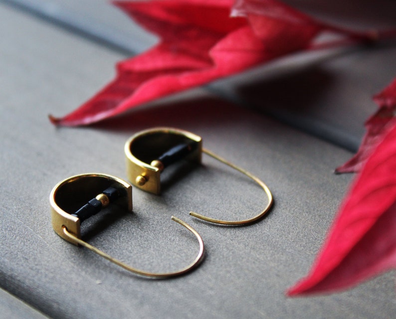 May include: A pair of gold hoop earrings with black accents. The earrings are made of a thin metal and have a simple design.