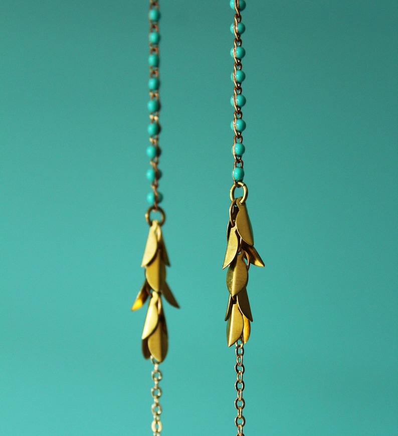 May include: A pair of gold earrings with turquoise beads and a dangling chain of gold leaves.