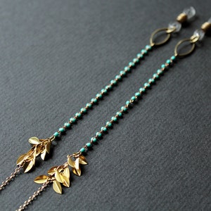 May include: A pair of turquoise beaded eyeglass chains with gold leaf accents. The chains are attached to clear plastic earpieces.