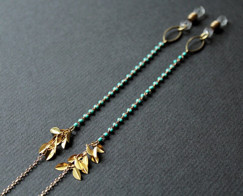 May include: A pair of turquoise beaded eyeglass chains with gold leaf accents. The chains are attached to clear plastic earpieces.