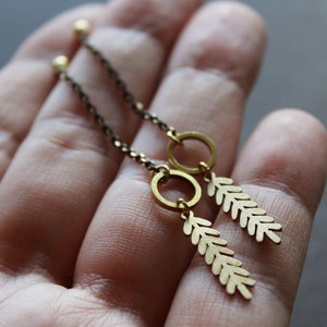 May include: A pair of gold-toned earrings with a delicate chain and a leaf-shaped pendant. The earrings are hanging from a hand.