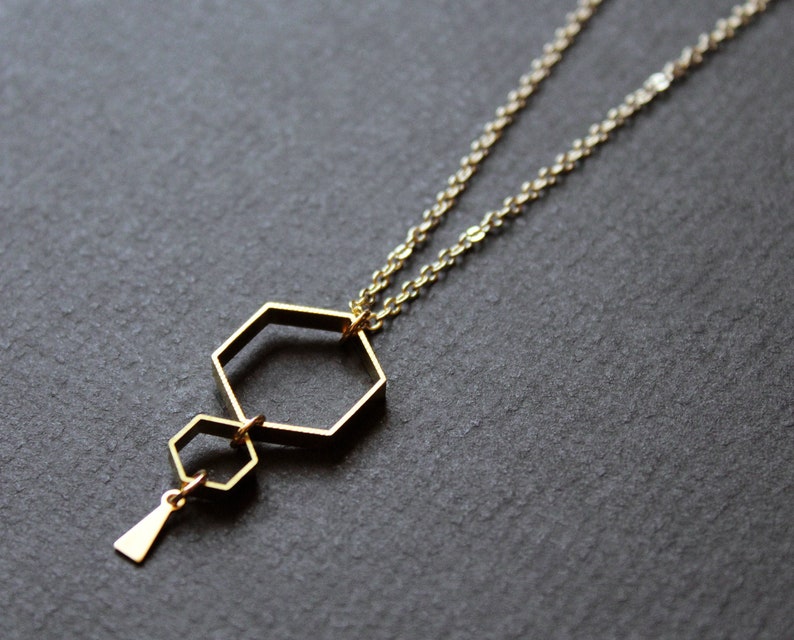 May include: A gold necklace with a geometric pendant featuring two interlocking hexagonal shapes.
