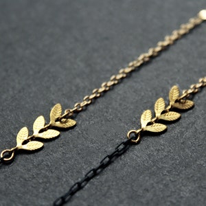 May include: Two gold chains with leaf-shaped charms. The chain on the top is a lighter gold color and the chain on the bottom is a darker gold color.
