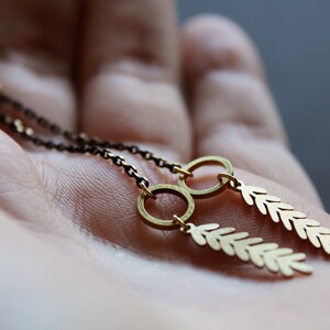 May include: A pair of gold earrings with delicate leaf-shaped charms hanging from small hoops. The earrings are on a hand, with the chain visible.