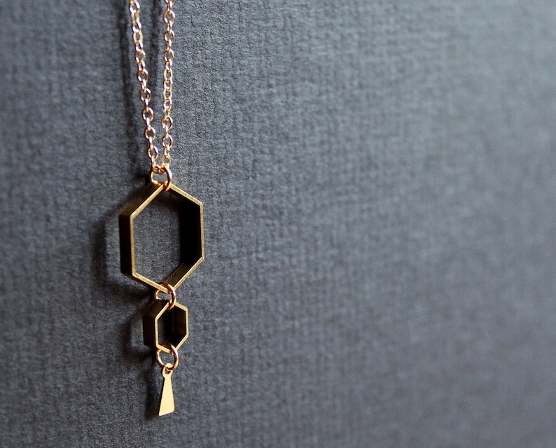 May include: A gold necklace with a geometric pendant featuring three connected hexagonal shapes.
