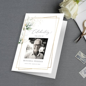 以下が含まれることがあります： 金色の枠と緑の葉が付いた白いカード。 「Celebrating the Life of」というテキストが黒い筆記体で書かれています。 カードの中央には男性の白黒写真があります。 「Mitchell Hodder June 19, 1942 - March 23, 2024」というテキストが写真の真下に黒で書かれています。