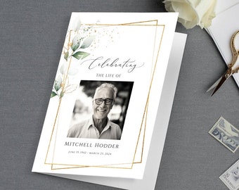 May include: A white card with a gold frame and green leaves. The text "Celebrating the Life of" is written in black cursive. A black and white photo of a man is in the center of the card. The text "Mitchell Hodder June 19, 1942 - March 23, 2024" is written in black below the photo.