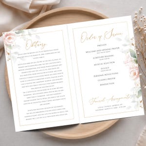 K&ouml;nnte beinhalten: Ein gefaltetes Trauerprogramm mit goldenen Schreibschrift-&Uuml;berschriften f&uuml;r Obituary und Order of Service. Das wei&szlig;e Papier zeigt schwarzen Text &uuml;ber das Leben von Judith Ann Thompson, akzentuiert durch rosa Aquarellrosen und gr&uuml;nes Blattwerk.