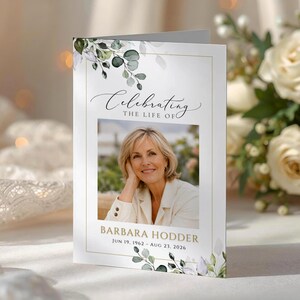 May include: A folded funeral program card featuring a white background with gold border lines and green watercolor eucalyptus leaves. The text reads Celebrating THE LIFE OF, BARBARA HODDER, and JUN 19, 1962 - AUG 23, 2026, with a central photo.