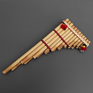 May include: A traditional wooden panpipe, also known as a Quena, with red and white string accents and colourful tassels. The panpipe is made of natural bamboo and is a popular instrument in Andean music.
