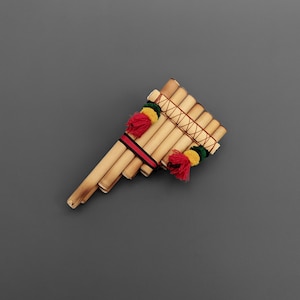 May include: A wooden panpipe with red, yellow, and green tassels. The panpipe is made of natural bamboo and has a rustic look.