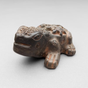 May include: A dark brown ceramic frog figurine with intricate details and a textured surface.