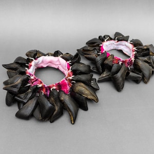 May include: Two black and brown bracelets made of shark teeth, each with a pink and red fabric lining.