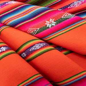 Op de afbeelding: Een close-up van kleurrijke geweven stof met oranje, roze, groene, blauwe en witte strepen. De stof is gevouwen en gelaagd, waardoor een textuurrijk en ingewikkeld patroon ontstaat.