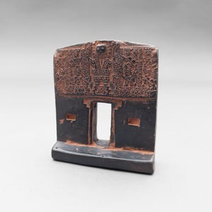 Peut inclure: Une petite sculpture en céramique noire représentant une porte avec des sculptures complexes. La porte est encadrée par deux piliers et possède une petite fenêtre au centre. La sculpture est décorée de motifs géométriques et de symboles.