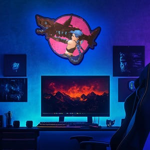 May include: A blue and pink neon sign with a female character holding a large shark. The sign is mounted on a wall in a gaming room with a computer monitor, a gaming chair, and other decor.