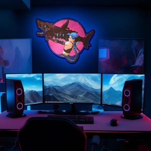 May include: A gaming setup with three monitors displaying mountain landscapes, two black speakers, and a pink and blue neon sign with a female character holding a weapon.