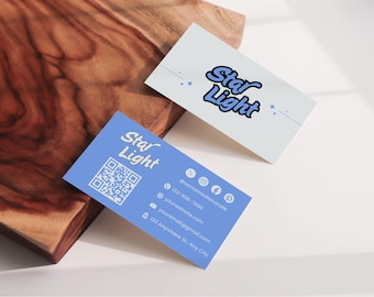 Könnte beinhalten: Zwei Visitenkarten mit dem Text "Star Light" in einer stilisierten Schriftart. Eine Karte ist hellblau mit einem QR-Code und Kontaktinformationen. Die andere Karte ist weiß. Beide Karten liegen auf einer Holzoberfläche.
