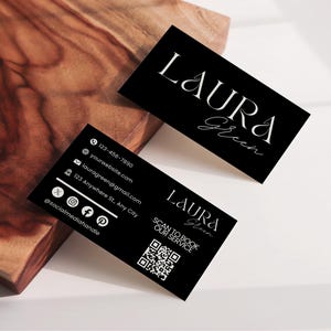 Peut inclure: Cartes de visite noires avec le nom "LAURA Green" en écriture blanche. Une carte affiche les coordonnées, dont un numéro de téléphone, un e-mail, un site Web et des identifiants de réseaux sociaux. Un code QR est également présent. Les cartes sont sur une surface en bois.