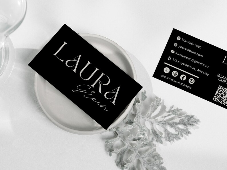 Op de afbeelding: Zwarte visitekaartjes met witte tekst, met de naam "LAURA Green" in elegante lettertypen. E&eacute;n kaart ligt op een wit bord, terwijl een andere contactgegevens weergeeft, waaronder een telefoonnummer, website en social media handle.
