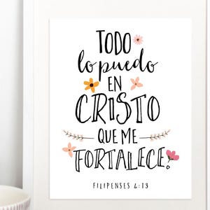 May include: A framed print with the Spanish text "Todo lo puedo en Cristo que me fortalece" in black script, accented with floral illustrations. The print is displayed on a wooden surface with a decorative tray and a small plant.