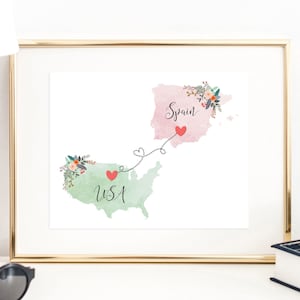 May include: A watercolor print of a map of Spain and the USA connected by a dotted line with hearts. The map of Spain is pink and the map of the USA is green. The text "Spain" and "USA" are written on the maps.
