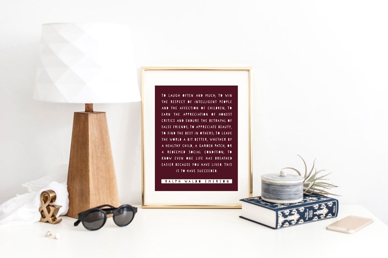 May include: A framed print with a burgundy background and white text. The quote reads: "To laugh often and much, to win the respect of intelligent people and the affection of children, to earn the appreciation of honest critics and endure the betrayal of false friends; to appreciate beauty, to find the best in others, to leave the world a bit better, whether by a healthy child, a garden patch, or a redeemed social condition; to know even one life has breathed easier because you have lived, this is to have succeeded." The quote is attributed to Ralph Waldo Emerson.