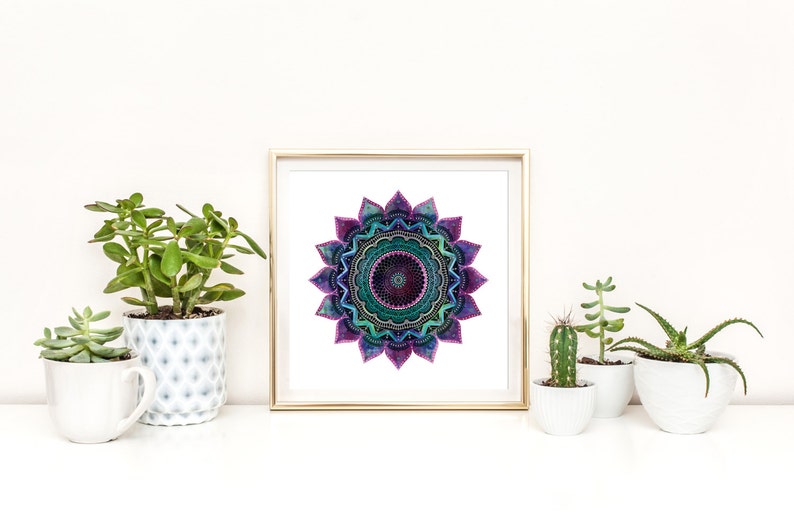 May include: A framed print of a colorful mandala with a purple, green, and blue color scheme. The mandala is surrounded by a white background and a gold frame. The print is displayed on a shelf with several potted plants.