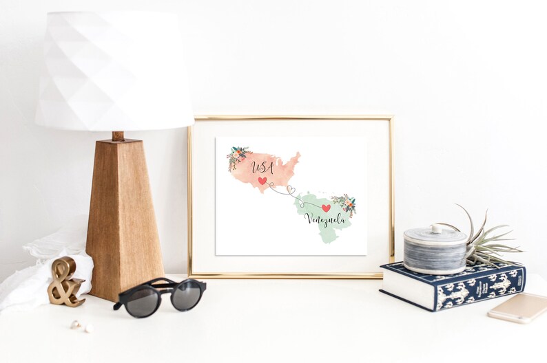 May include: A framed print with a watercolor map of the USA and Venezuela connected by a dotted line with hearts. The USA is in peach and Venezuela is in green. The text "USA" and "Venezuela" are written on the map.