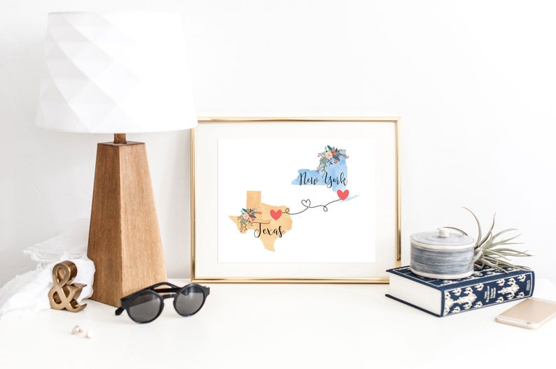 K&ouml;nnte beinhalten: Ein goldfarbener Druck mit einer Aquarell-Illustration der Bundesstaaten Texas und New York, die durch eine Linie mit Herzen verbunden sind. Der Text "Texas" und "New York" steht auf den Bundesstaaten.