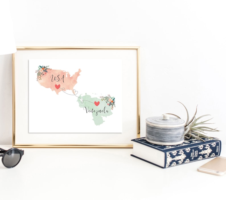 May include: A watercolor print of a map of the USA and Venezuela connected by a dotted line with hearts. The USA is pink and Venezuela is green. The words "USA" and "Venezuela" are written on the map.