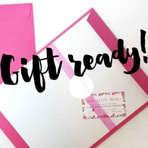 May include: A pink envelope with a white envelope inside. The white envelope has a pink stripe across it and the text "Gift ready!" in black. The white envelope also has a small business card with the text "Mad Kitty Media" on it.