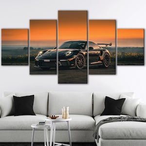 Könnte beinhalten: Ein fünfteiliges Wandbild-Set, das einen schwarzen Sportwagen mit Heckflügel im Freien zeigt. Die Szene fängt das Fahrzeug bei Sonnenuntergang mit einem leuchtend orangefarbenen Himmel und einer dunklen Horizontlinie ein. Das Auto ist mittig platziert und präsentiert seine Scheinwerfer, Leichtmetallfelgen und aerodynamische Karosserie vor dem warmen, leuchtenden Hintergrund des Abendlichts.
