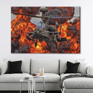 May include: A military helicopter, painted in shades of green and gray, is captured mid-flight against a backdrop of an intense explosion. The scene is dominated by fiery orange and black smoke, creating a dramatic contrast.