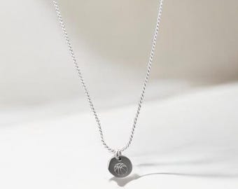 May include: A silver necklace with a delicate chain and a small, round pendant. The pendant features a palm tree design. The necklace is displayed against a white background, highlighting its simple elegance and minimalist style.