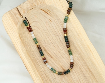 May include: A beaded necklace featuring a repeating pattern of small, round, polished stones in shades of forest green, deep brown, and translucent white, interspersed with thin, flat, gold-toned metal spacers along the entire length of the strand.