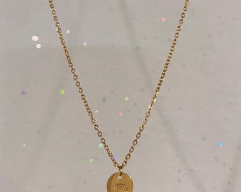 May include: A gold-colored necklace with a delicate chain and a circular pendant. The pendant features a small engraved rainbow design. The necklace is displayed against a white background with sparkling accents, creating a simple and elegant aesthetic.