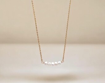 May include: A delicate gold chain necklace with a row of five small white pearls.