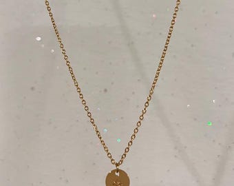 May include: A delicate gold-colored necklace featuring a fine chain and a circular pendant. The pendant has a starburst design. The necklace is displayed against a light background, highlighting its simple elegance. A piece of jewelry.