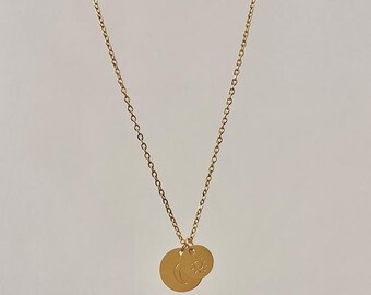 May include: Gold-colored necklace featuring a delicate chain and two circular pendants. One pendant displays a crescent moon, and the other features a sun design. The necklace is a simple, elegant piece of jewelry.