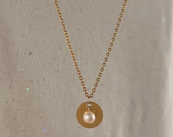 May include: A gold chain necklace with a small round pendant featuring a heart design and a single pearl.