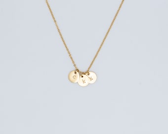 May include: A gold-colored necklace with three circular pendants. Each pendant has a single letter engraved on it: "C", "K", and "K". The necklace chain and pendants are a shiny gold color, set against a white background.