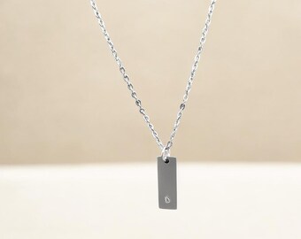 May include: A silver chain necklace with a small rectangular pendant that has the letter 'D' engraved on it.