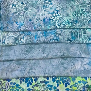 May include: A stack of five fabric squares with different blue and green patterns. The top square has a white and blue floral pattern, the next two squares are a solid blue, and the bottom two squares have a green and blue floral pattern.