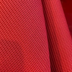 May include: Red fabric with a textured diamond pattern. The fabric is folded in half, showing the texture on both sides.