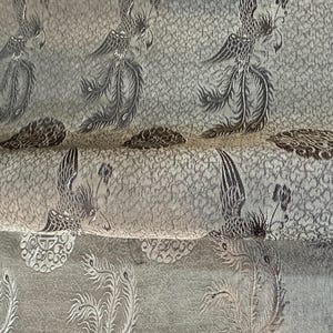 May include: Close-up of a fabric with a repeating pattern of stylized phoenixes in shades of gray and brown. The fabric has a textured background with a subtle, swirling design. The phoenixes are detailed with intricate feather patterns.