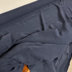 May include: A close-up of a dark blue fabric with a textured surface. The fabric is folded and draped, showing its soft and flowing texture.