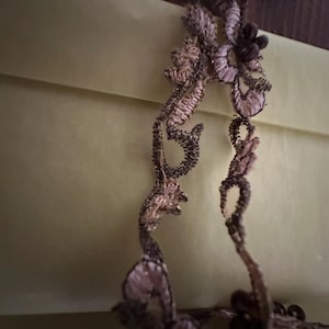 May include: A delicate lace trim with a floral design in shades of brown and pink. The lace is adorned with small, dark brown beads.