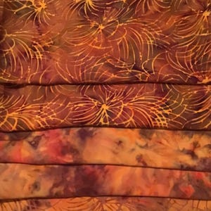 May include: A close-up of a stack of fabric with a brown and orange floral pattern. The fabric is folded in a way that shows the different layers of the pattern.