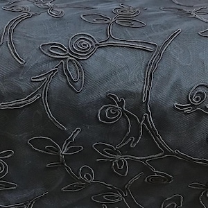 May include: Black sheer fabric with an embossed floral pattern. The fabric has a delicate, almost translucent quality.